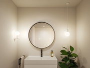 Modernes Badezimmer mit rundem Spiegel, weißem Waschbecken und zwei weißen Leuchten für stimmungsvolle Beleuchtung