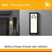 Black solar house number sign with white LED light on grey wall for energy-saving outdoor lighting