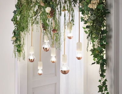 Hanging LED bulbs with copper tips and green foliage as decorative indoor lighting design.