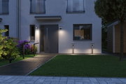 Modern black outdoor wall and bollard lights illuminate the entrance area with garden path at dusk.