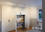 White built-in cabinet with integrated workspace, wooden shelves and black swivel stool in modern room