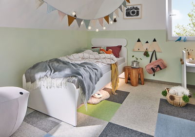 Child's room with white wooden bed, colorful carpet tiles, and decorative fabric bunting on wall