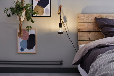 Modern wall lamp with wooden mount and black bulb beside rustic wooden bed in bedroom setting