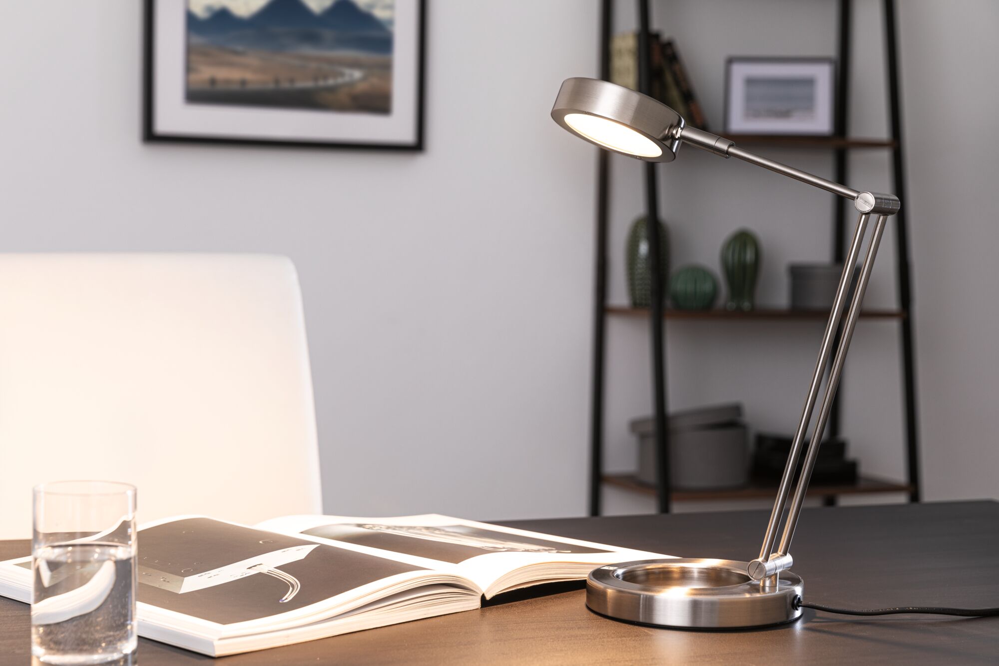 Modern LED desk lamp in brushed stainless steel with adjustable arm on office desk.