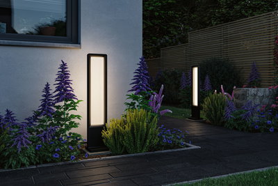 Lampes extérieures LED noires modernes en métal éclairent un chemin de jardin avec fleurs violettes et jaunes.