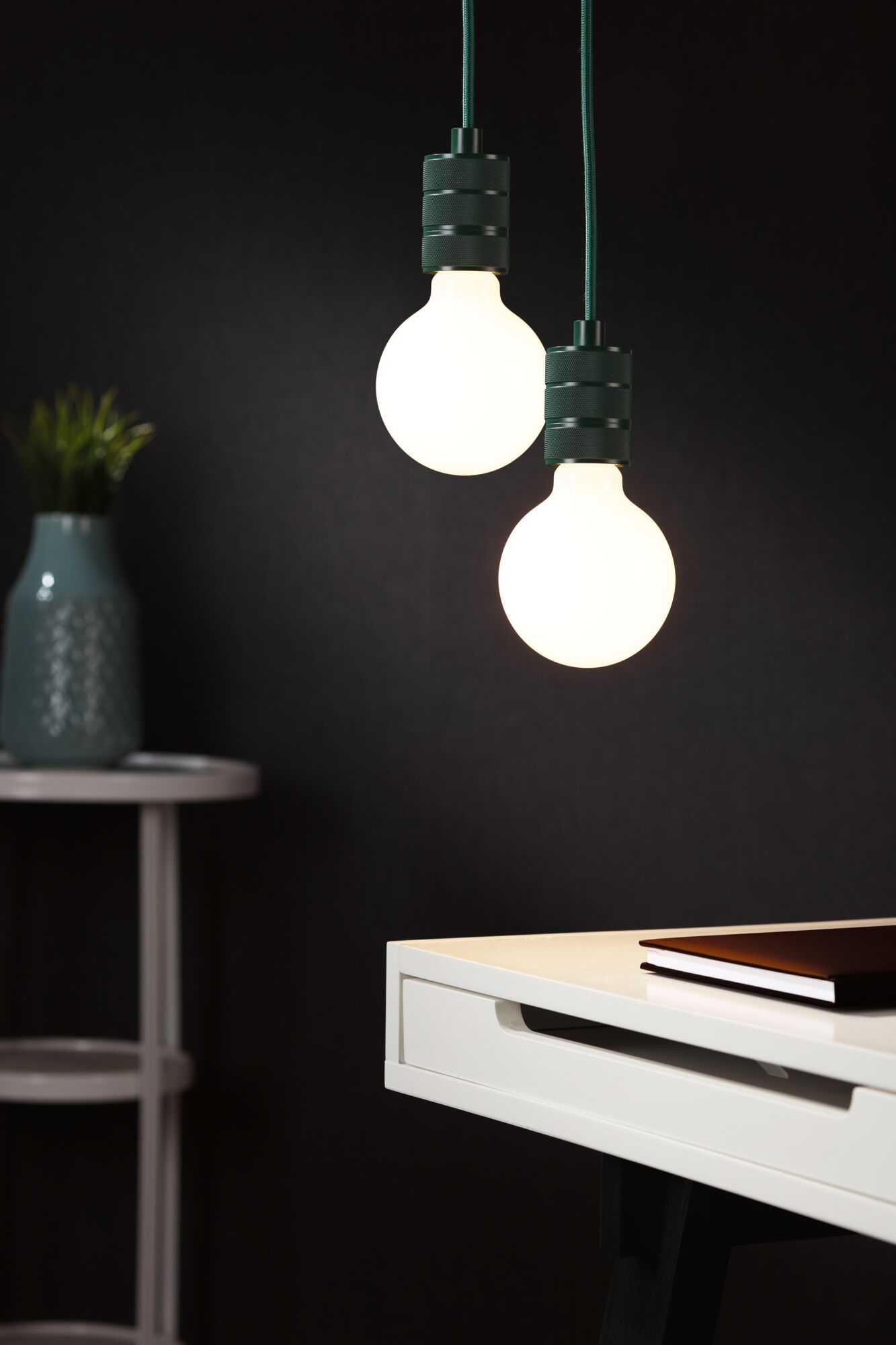 Twee hangende LED-lampen met zwarte metalen fittingen boven een wit bureau met boek, moderne verlichting.