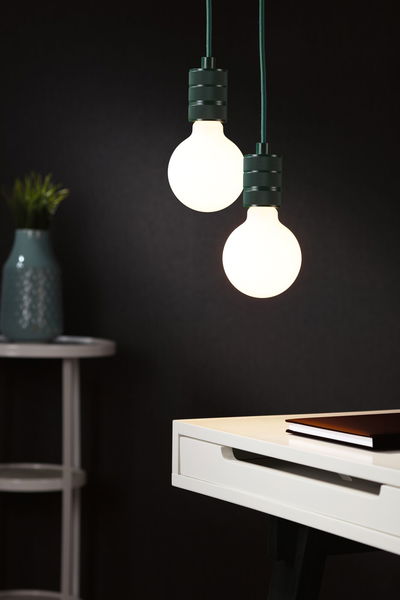 Twee hangende LED-lampen met zwarte metalen fittingen boven een wit bureau met boek, moderne verlichting.