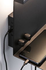 Schwarzes Metall-Wandregal mit zwei geriffelten Drehknöpfen und Smartphone mit USB-Ladekabel.