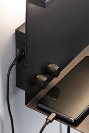Black metal wall shelf with two textured knobs and smartphone connected via USB charging cable.