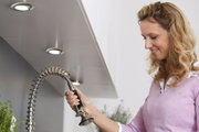 Woman using flexible stainless steel kitchen faucet with spring coil and spray head in modern kitchen