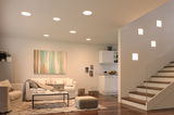 Modern living room with white recessed ceiling lights and square wall lamps by staircase, wooden floor