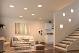 Modern living room with white recessed ceiling lights and square wall lamps by staircase, wooden floor