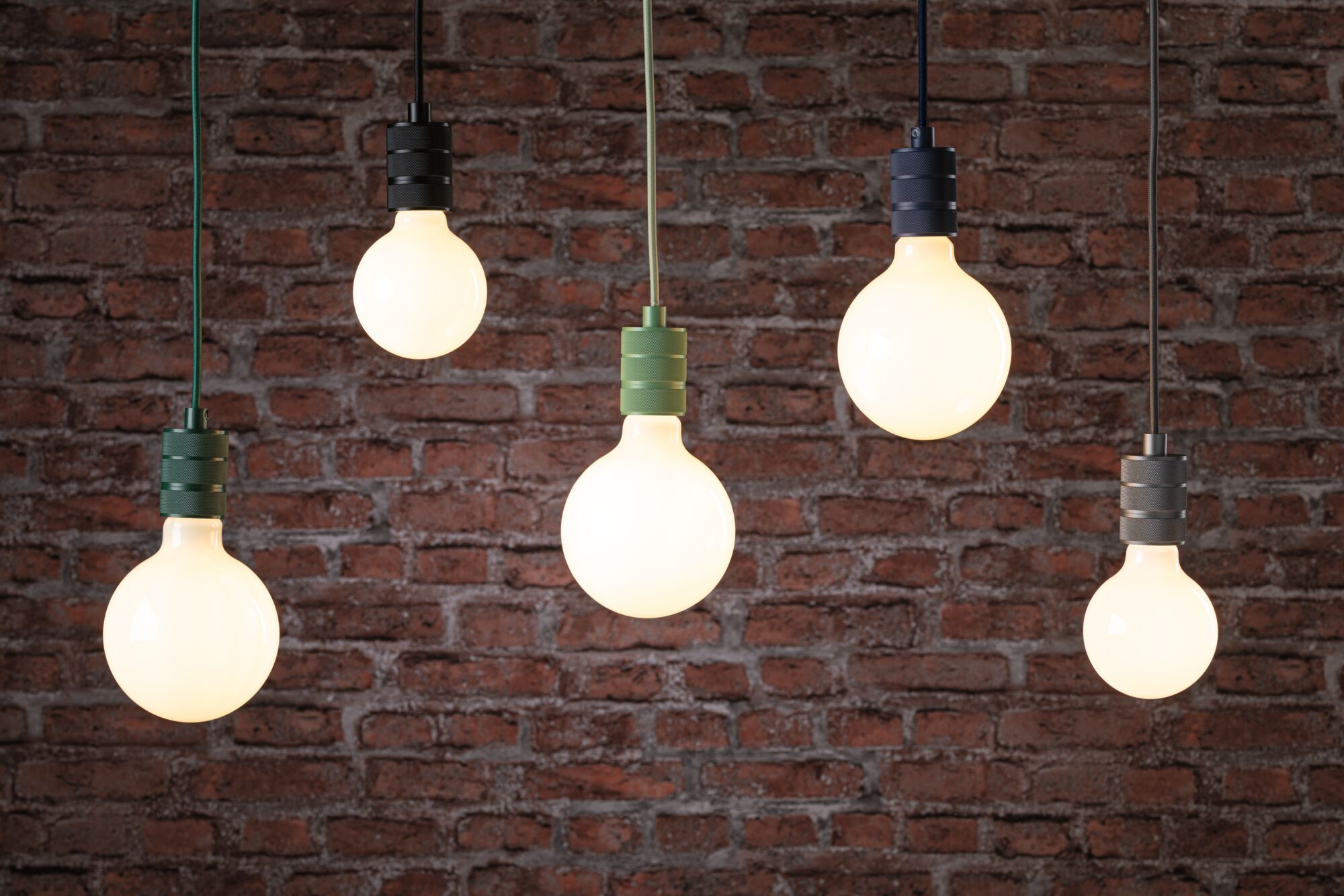 Five hanging LED bulbs with black, green, and gray sockets against red brick wall