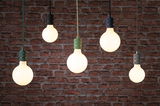 Five hanging LED bulbs with black, green, and gray sockets against red brick wall