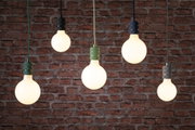 Vijf hangende lampen met zwarte en groene fittingen tegen een rode bakstenen muur, modern verlichtingsontwerp