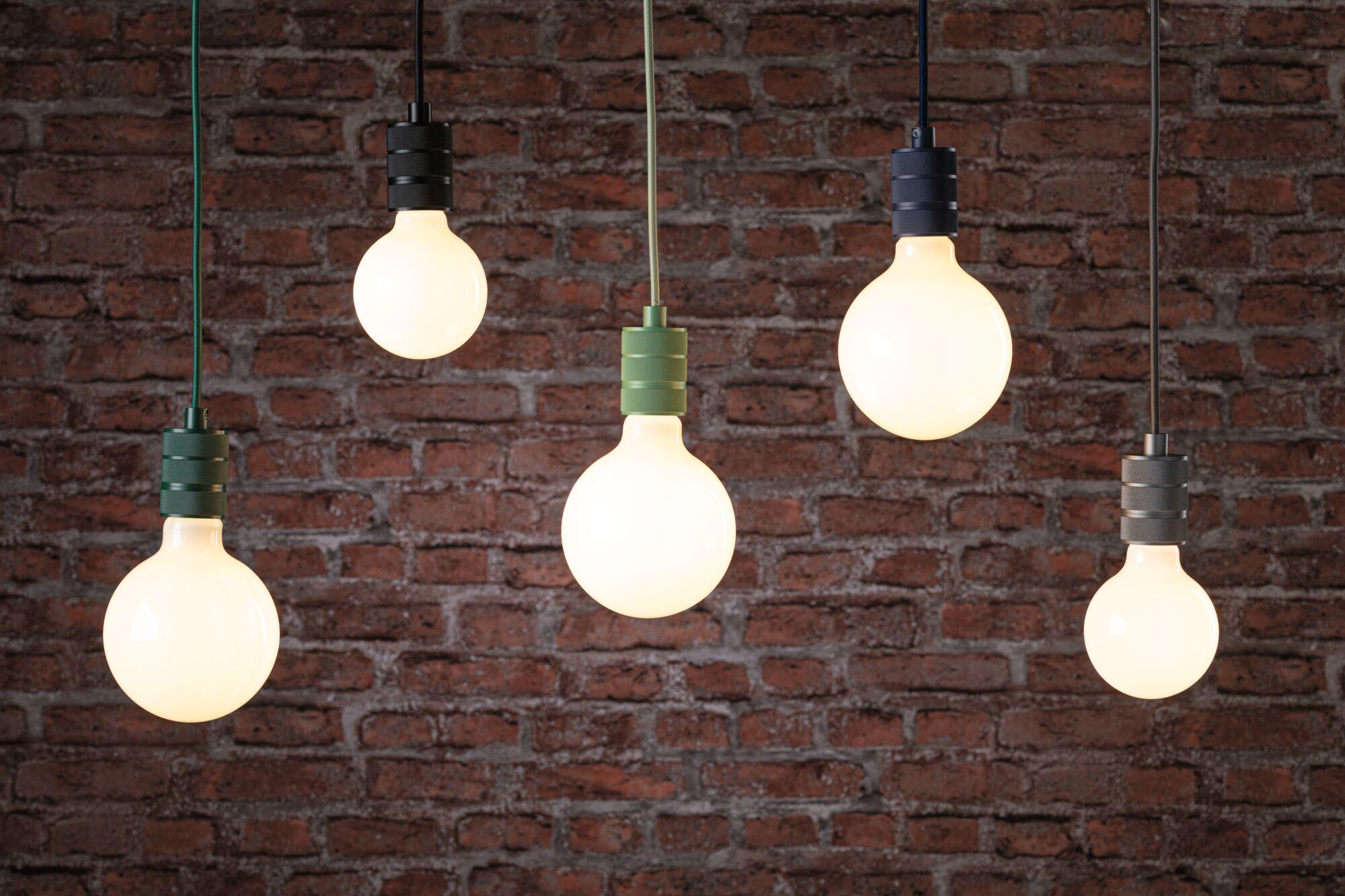 Vijf hangende lampen met zwarte en groene fittingen tegen een rode bakstenen muur, modern verlichtingsontwerp