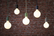 Vijf hangende lampen met zwarte en groene fittingen tegen een rode bakstenen muur, modern verlichtingsontwerp