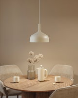 Beige metal pendant lamp above round wooden table with coffee pot and vase in dining room