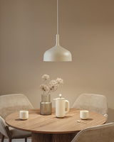 Beige metal pendant lamp above round wooden table with coffee pot and vase in dining room