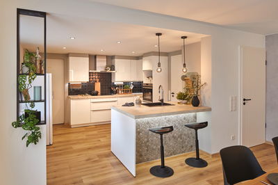 Modern white kitchen with wooden countertop, black backsplash, two black bar stools, and LED lighting