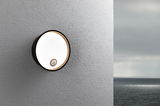 Round black outdoor wall light with motion sensor on grey wall, LED outdoor lamp by the sea