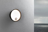 Round black outdoor wall light with motion sensor on grey wall, LED outdoor lamp by the sea
