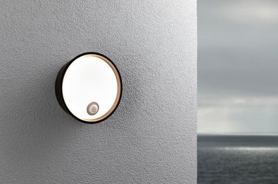 Runde schwarze Außenwandleuchte mit Bewegungsmelder an grauer Wand mit Meerblick, LED Außenlampe