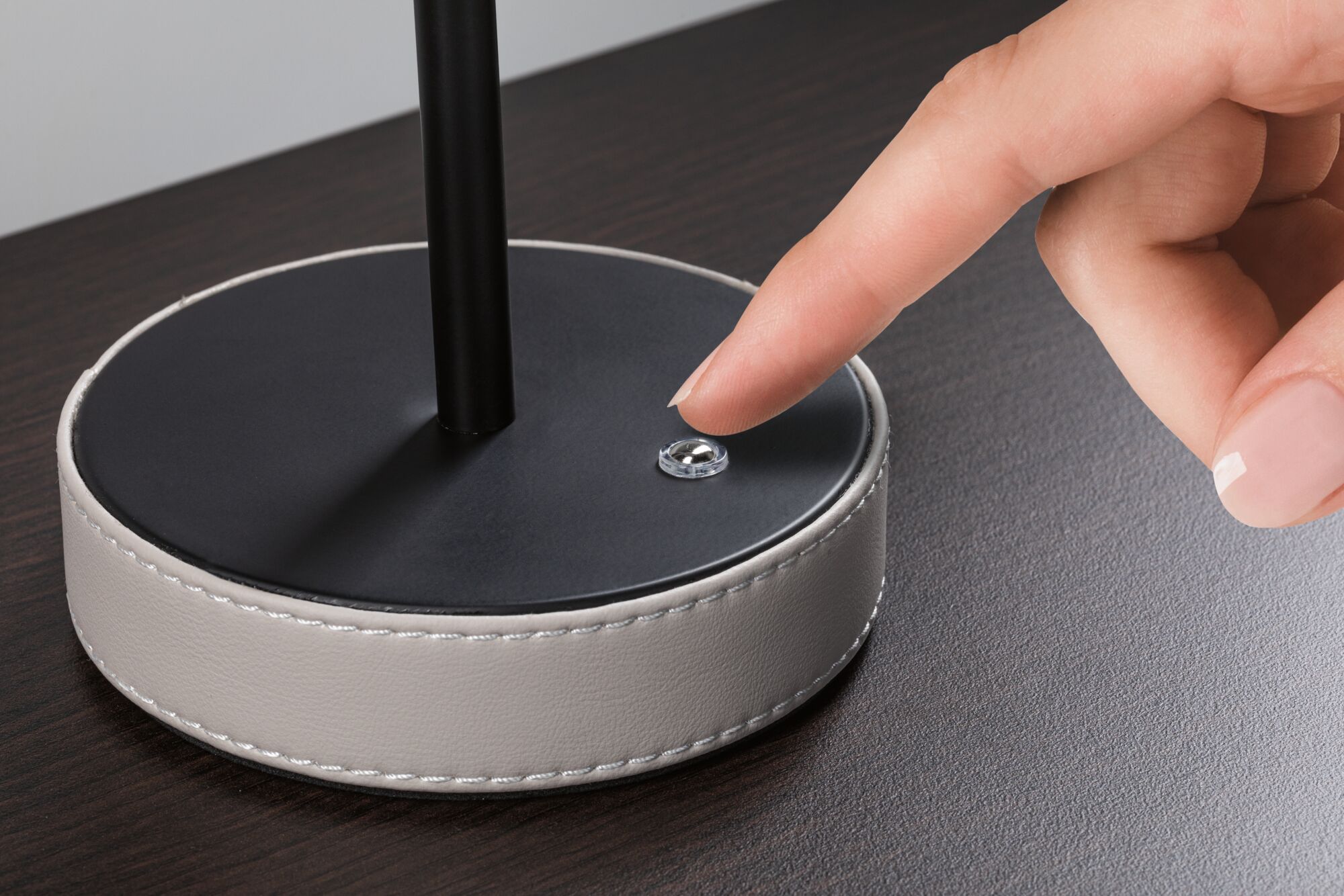 Black lamp base with white leather trim and finger pressing small round switch on dark table surface