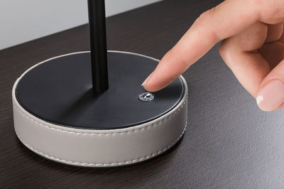 Black lamp base with white leather trim and finger pressing small round switch on dark table surface