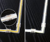 Bande LED avec connecteur d'angle transparent sur surface noire, lumière blanc chaud et vue détaillée.