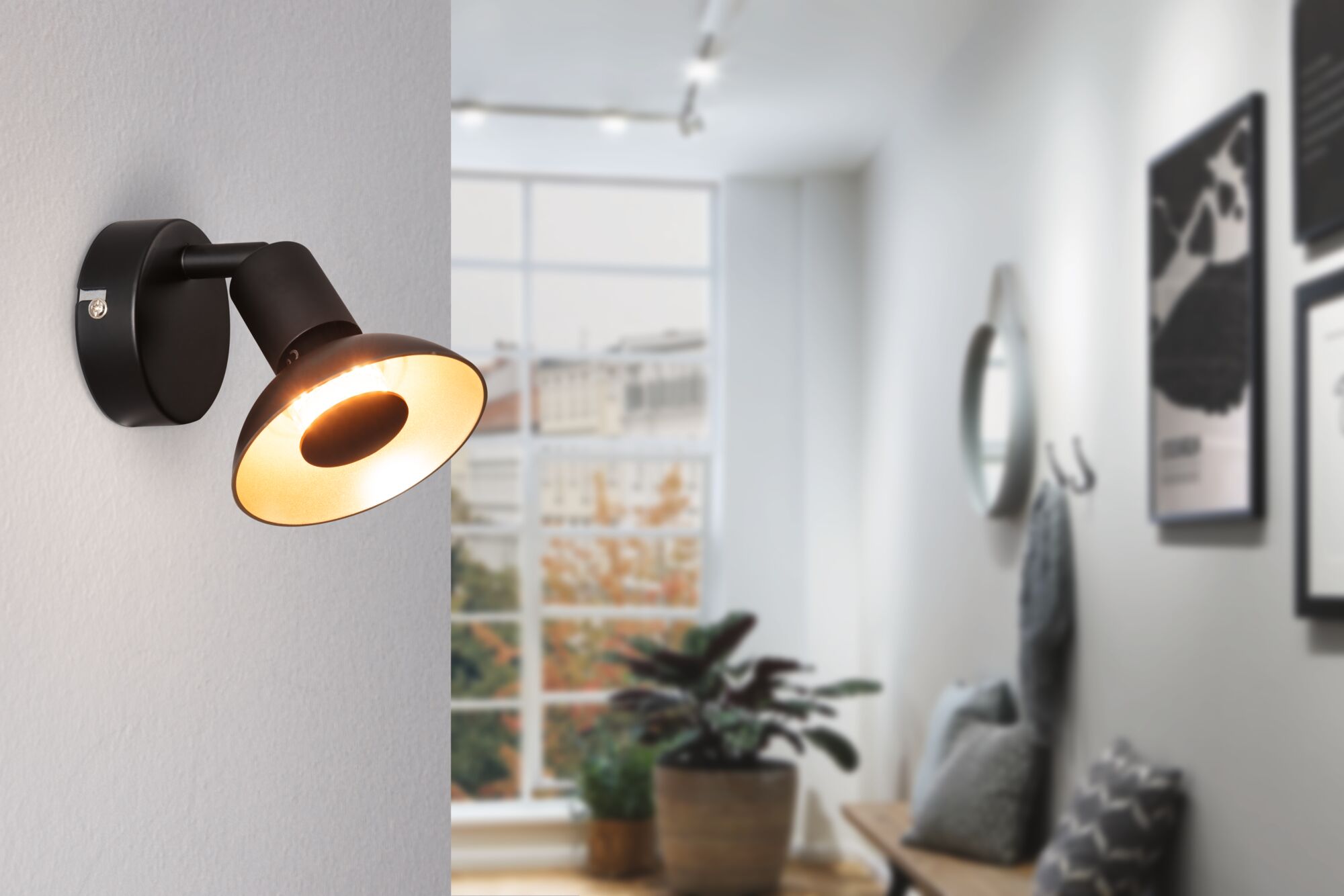 Black metal wall light with warm white glow in modern living room featuring window and plants