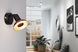 Black metal wall light with warm white glow in modern living room featuring window and plants