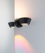 Applique murale noire en métal avec globe en verre diffusant une lumière chaude et des reflets colorés.