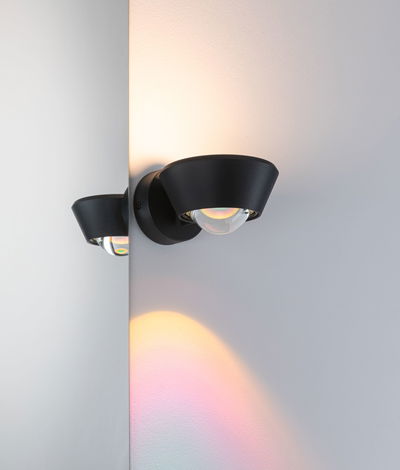 Applique murale noire en métal avec globe en verre diffusant une lumière chaude et des reflets colorés.