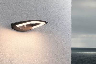 Moderne zwarte LED-buitenwandlamp met bewegingssensor op witte muur met zeezicht