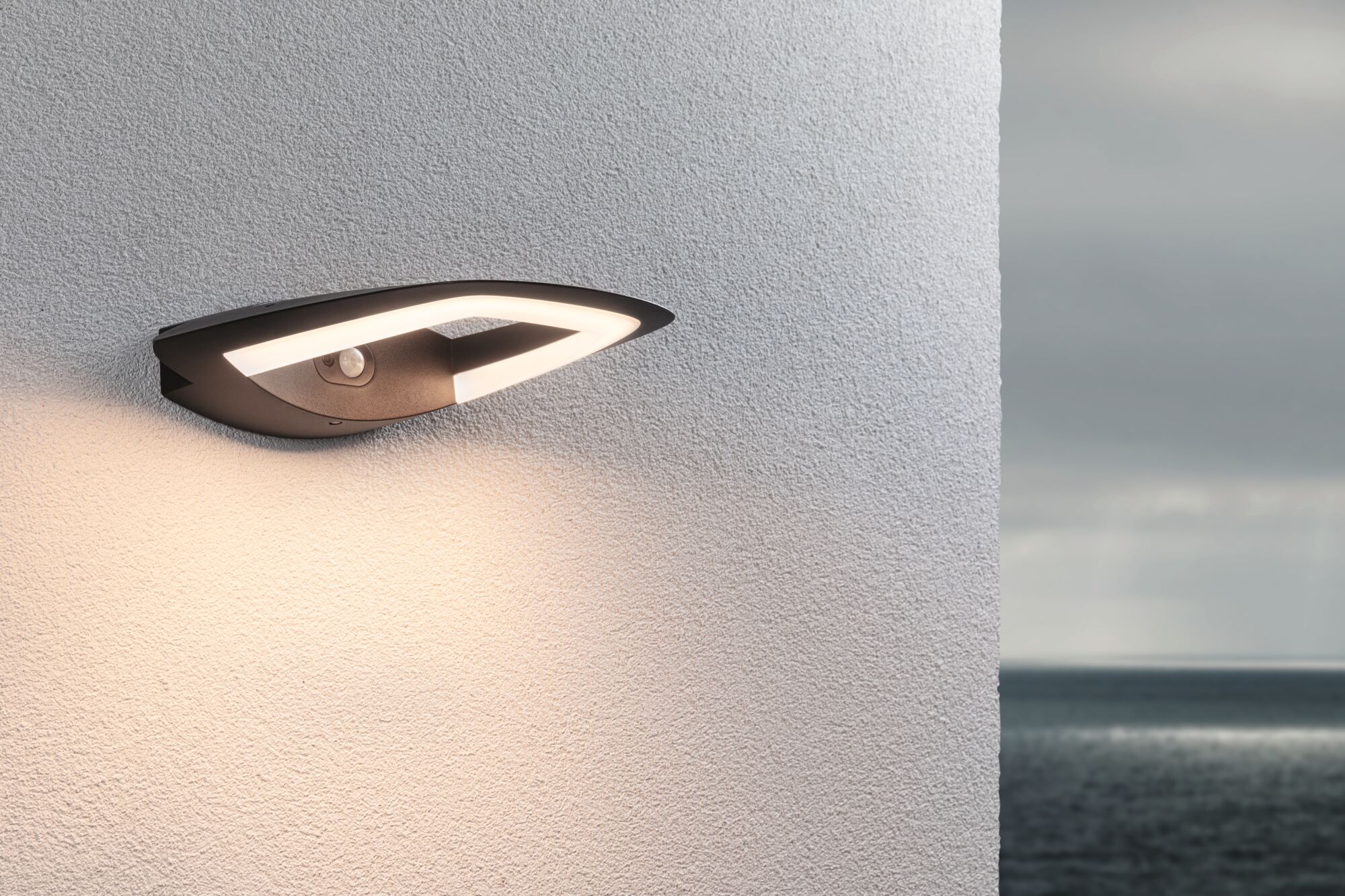 Moderne schwarze LED-Außenwandleuchte mit Bewegungsmelder an weißer Wand mit Meerblick
