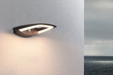 Moderne schwarze LED-Außenwandleuchte mit Bewegungsmelder an weißer Wand mit Meerblick