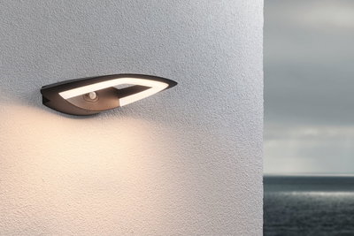 Moderne schwarze LED-Außenwandleuchte mit Bewegungsmelder an weißer Wand mit Meerblick