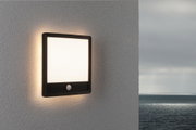 Black square outdoor wall light with motion sensor and warm white illumination on grey wall
