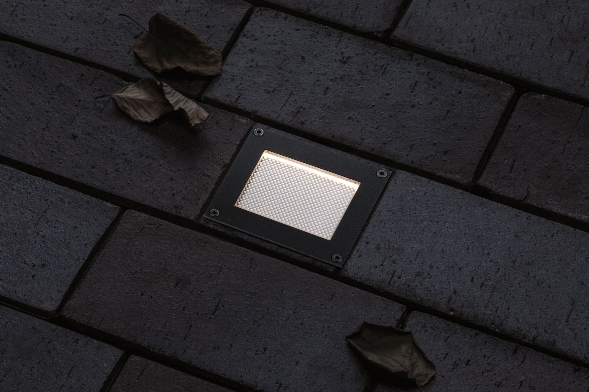 Rectangular black LED recessed floor light with warm white illumination on dark pavement.