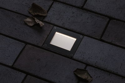Rectangular black LED recessed floor light with warm white illumination on dark pavement.