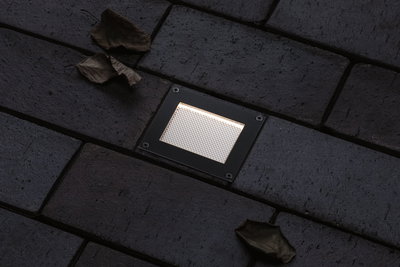 Rektangulært sort LED-indbygningsgulvlys med varmt hvidt lys på mørk belægning.