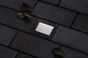 Square black metal LED floor light with warm white illumination on dark pavement surface