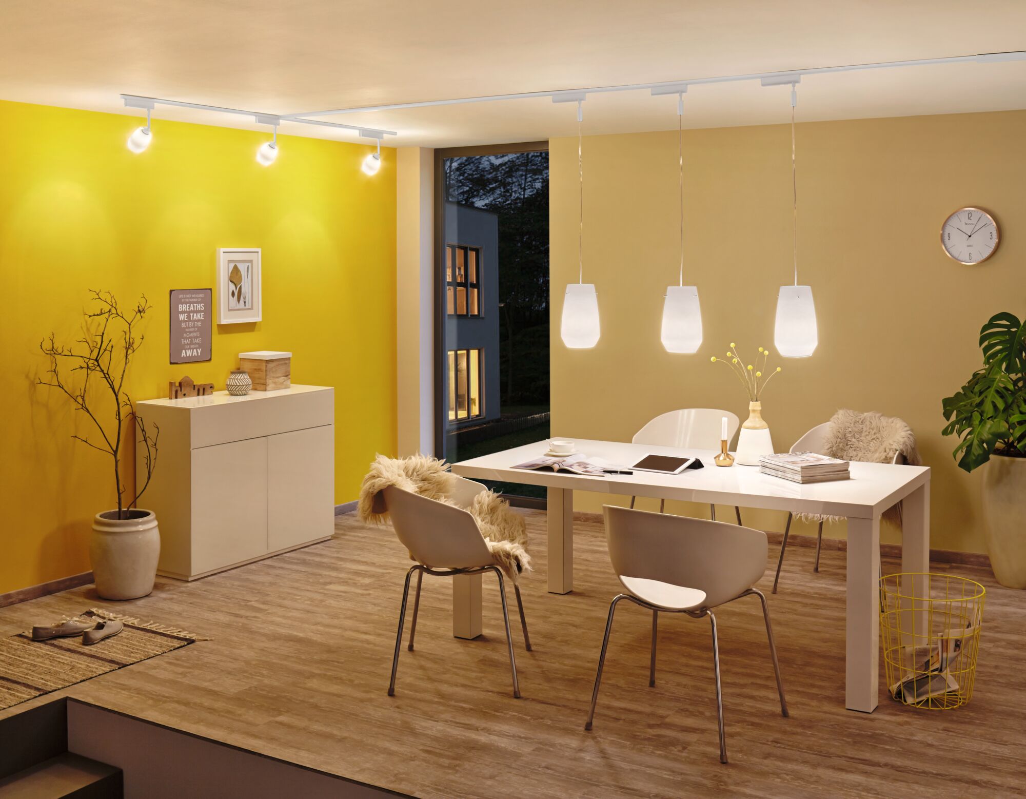 Modernes Esszimmer mit weißen Stühlen, Holzboden und drei weißen Pendelleuchten an der Decke.