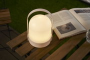 White portable LED table lamp with warm light on wooden table beside open book