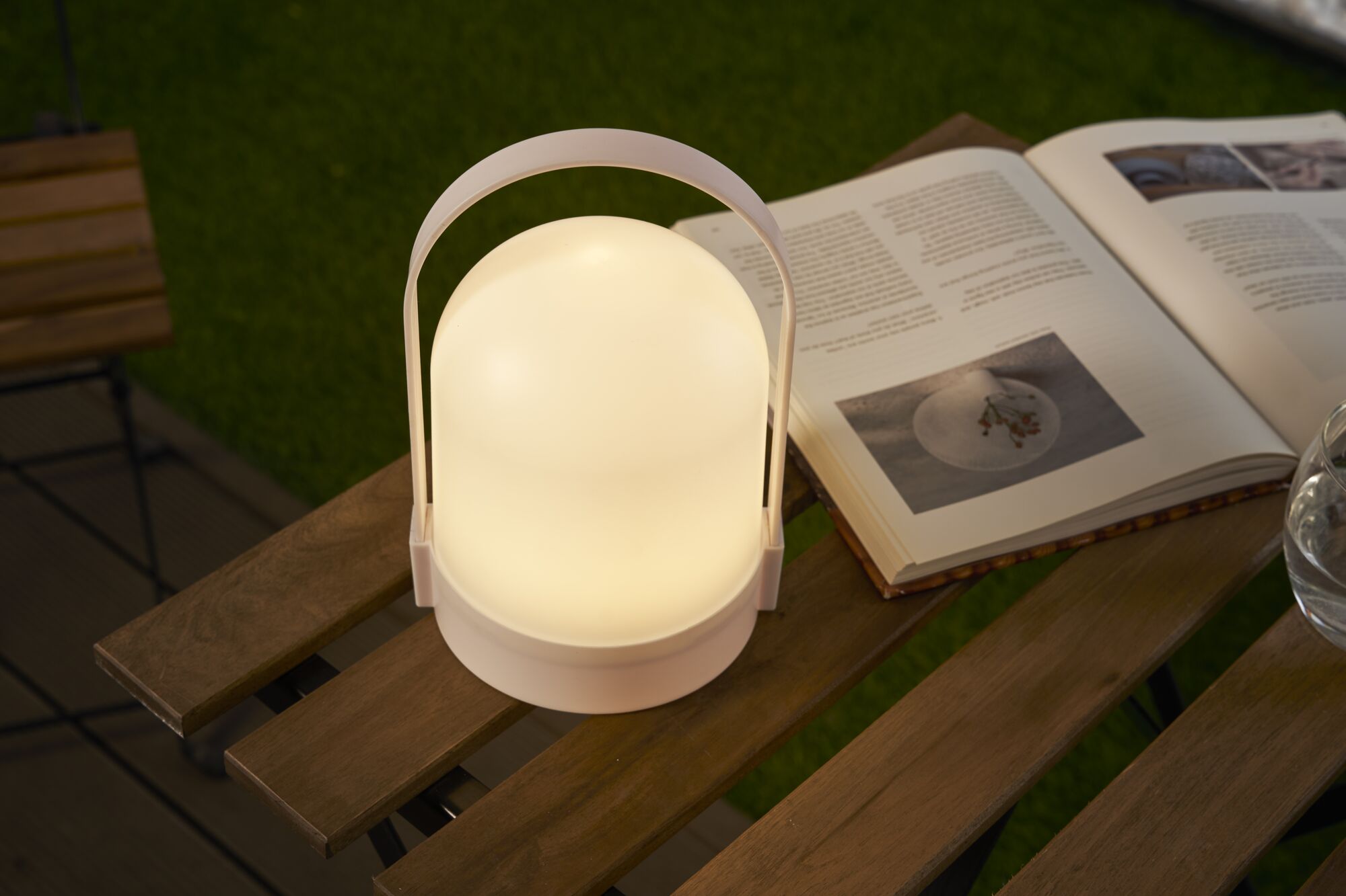 White portable LED table lamp with warm light on wooden table beside open book
