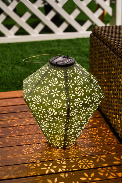 Groene solar lantaarn met bloemenpatroon van metaal op houten terras, decoratieve tuinverlichting.