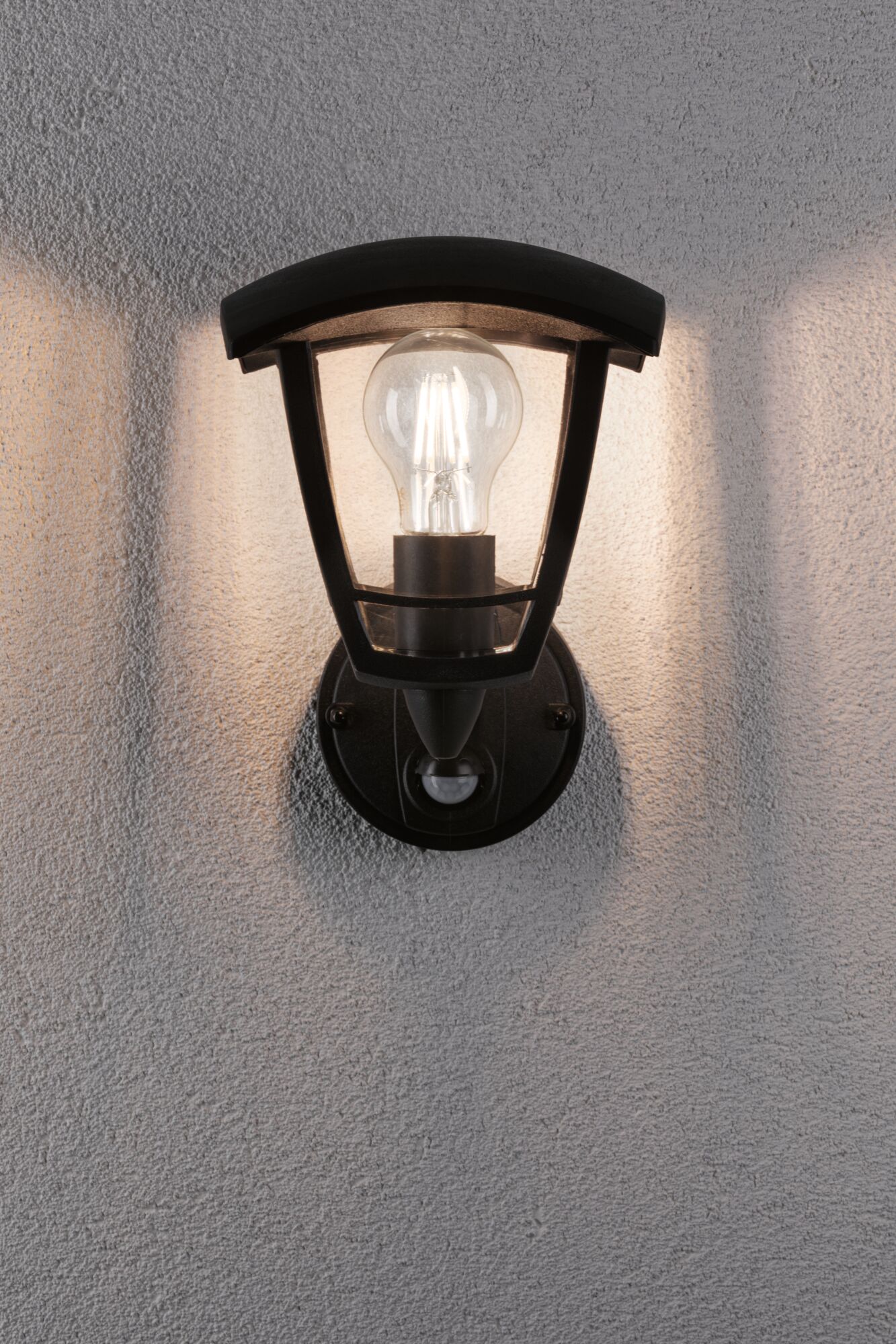 Schwarze Außenwandleuchte aus Metall mit klarem Glas und sichtbarer LED-Glühbirne an grauer Wand
