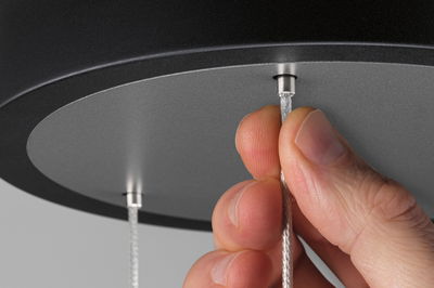 Hånd trækker sølvfarvet tekstilkabel ud af sort loftslampe med gråt indsats til LED-belysning