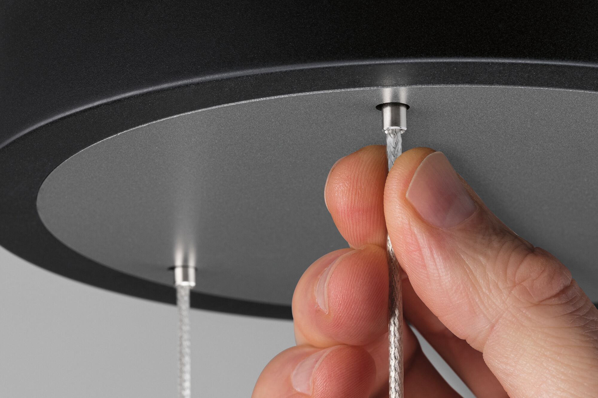 Main tirant un câble textile argenté d'un plafonnier noir avec insert gris pour éclairage LED